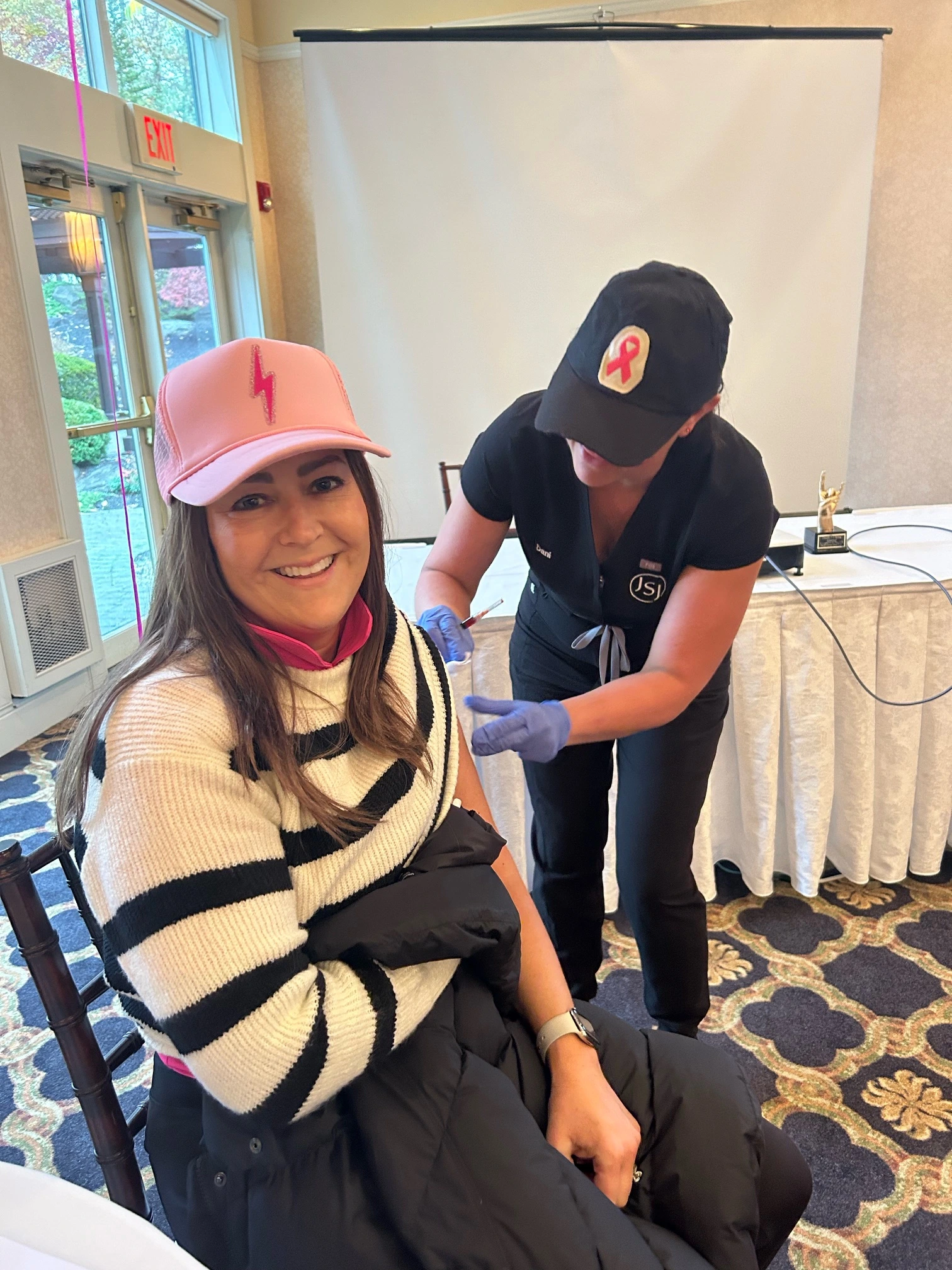 a woman sitting in a chair with a woman in a pink hat